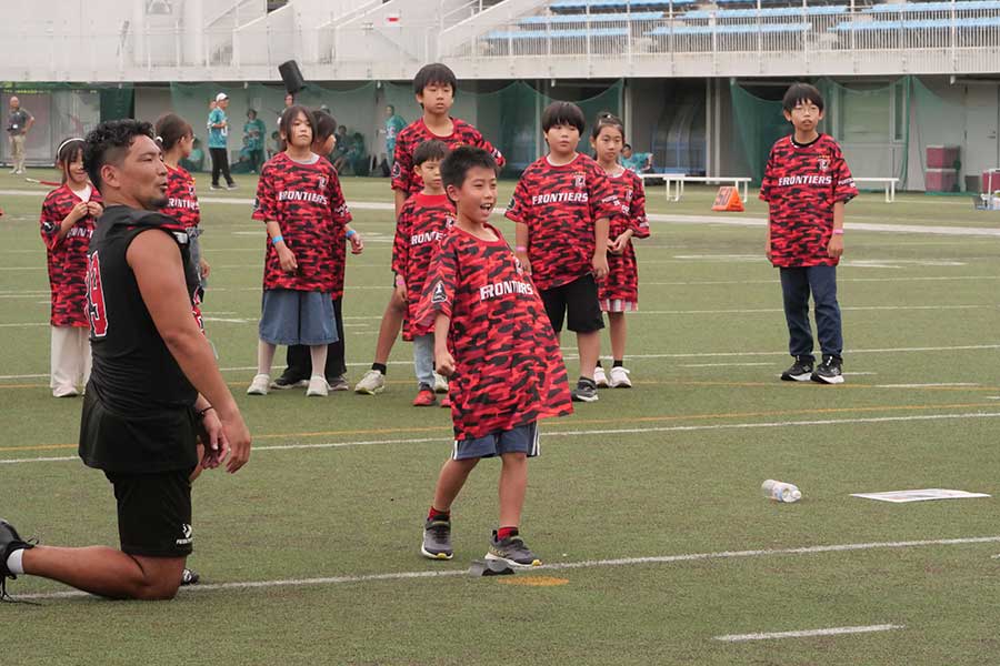 ボールをキックし、笑顔を見せる参加者の子供と見守る富士通アメリカンフットボール部・福井雄哉(左)【写真:上田悠太】